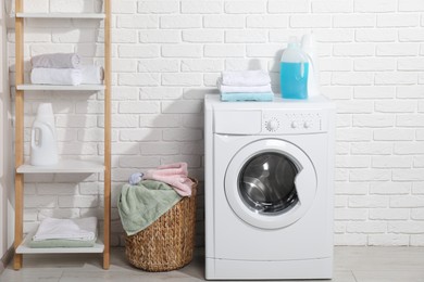 Photo of Laundry detergents and stacked clean towels on washing machine in bathroom