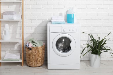 Photo of Laundry detergents and stacked clean towels on washing machine in bathroom