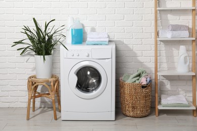 Photo of Laundry detergents and stacked clean towels on washing machine in bathroom