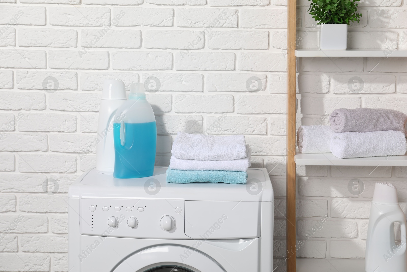 Photo of Laundry detergents and stacked clean towels on washing machine in bathroom