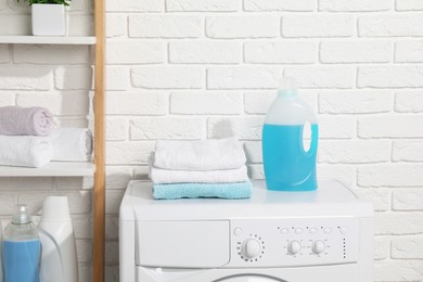 Photo of Laundry detergents and stacked clean towels on washing machine in bathroom