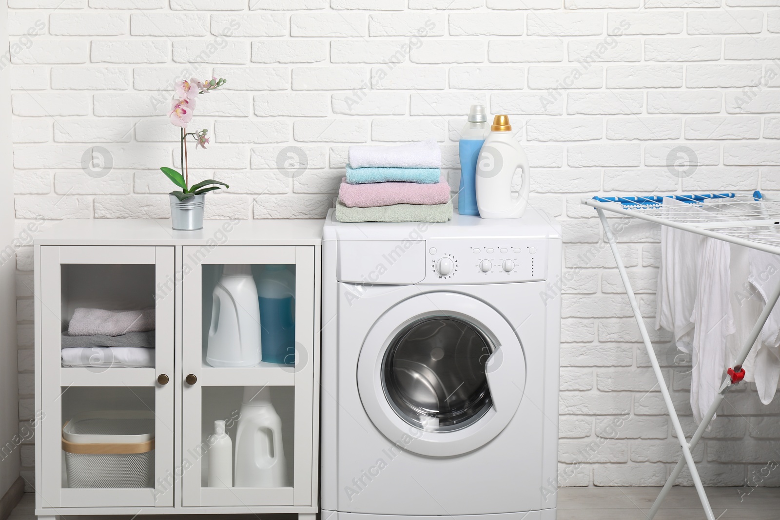 Photo of Laundry detergents and stacked clean towels on washing machine in bathroom