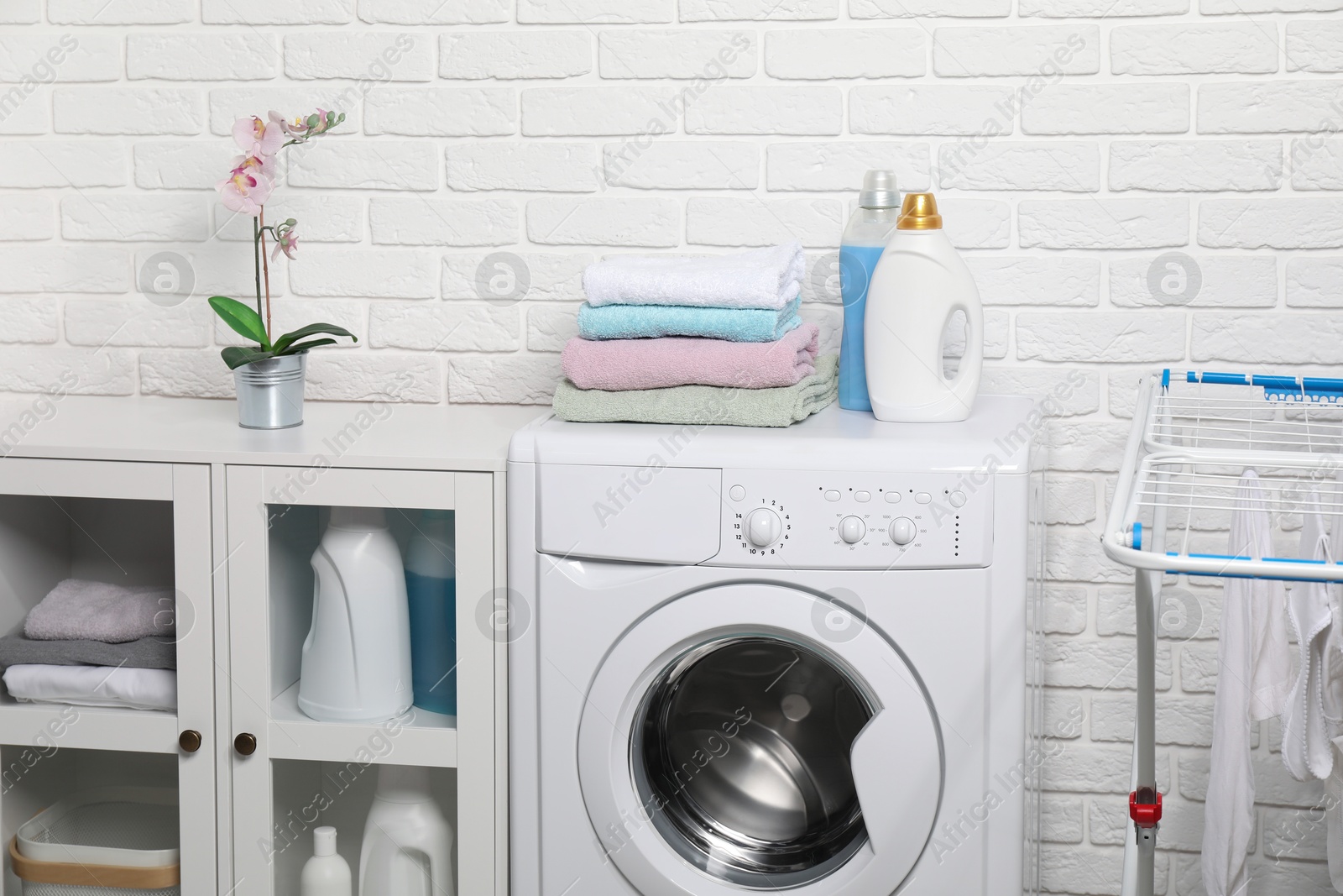 Photo of Laundry detergents and stacked clean towels on washing machine in bathroom