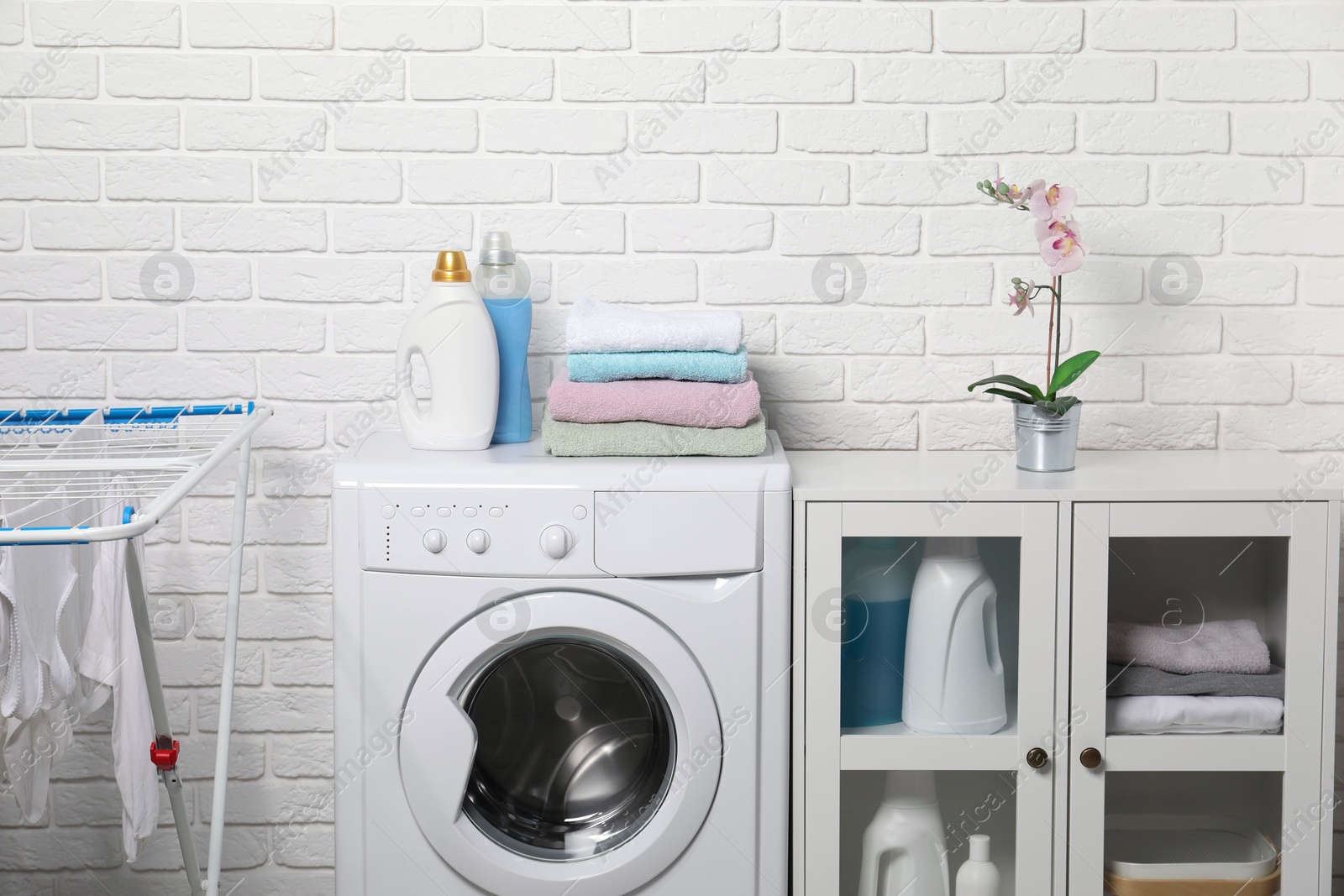 Photo of Laundry detergents and stacked clean towels on washing machine in bathroom