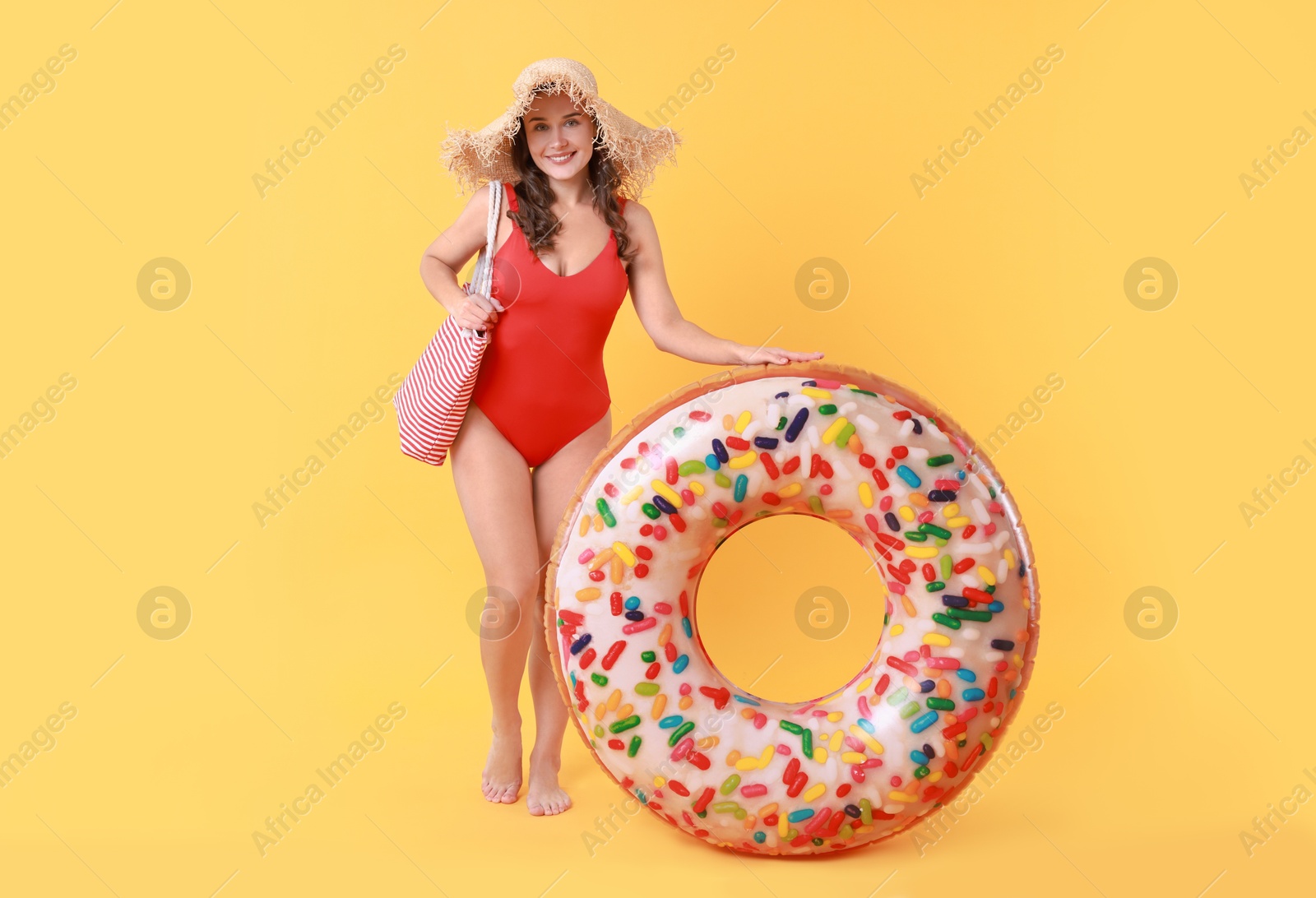 Photo of Beautiful woman wearing swimsuit and straw hat with inflatable ring on yellow background