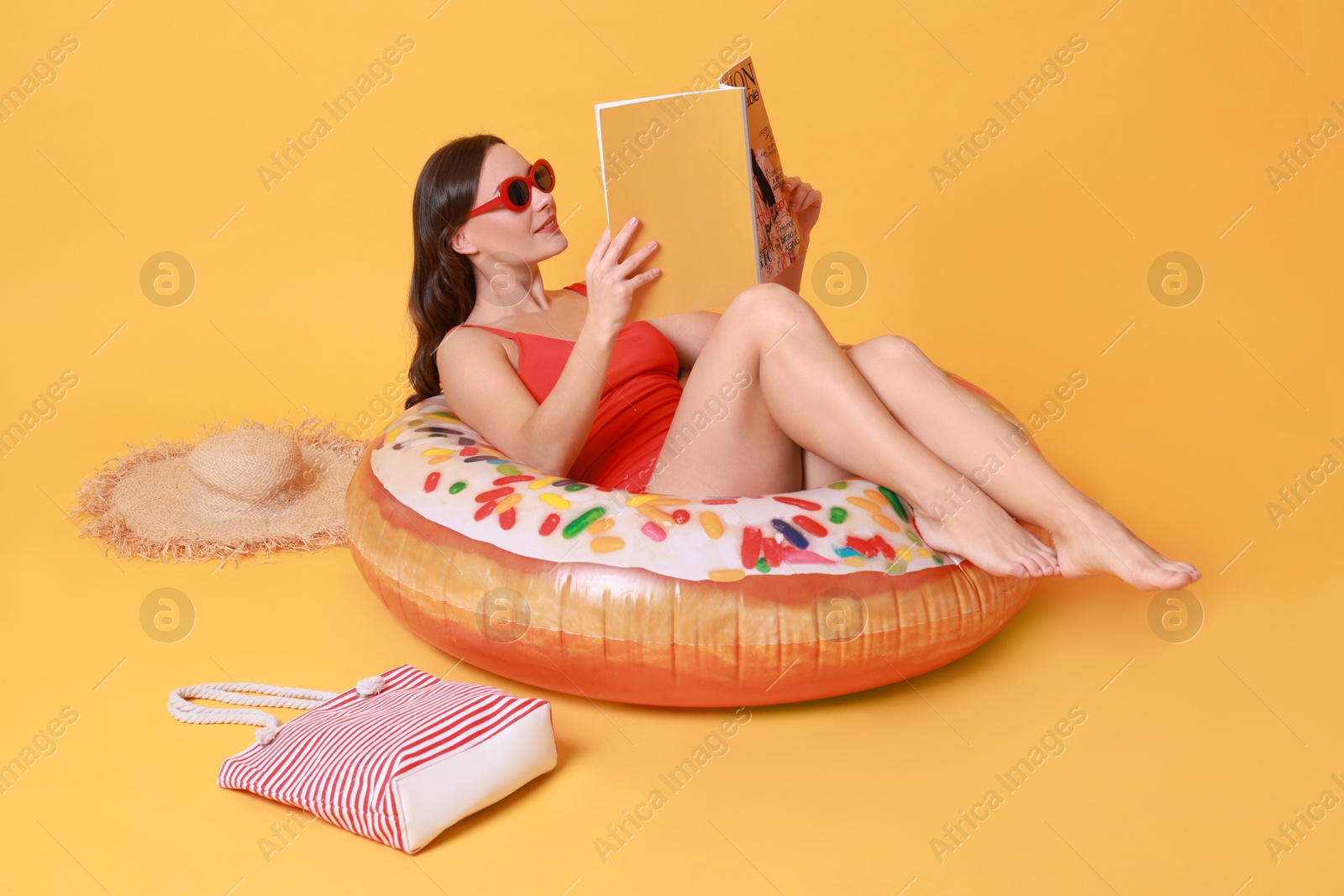 Photo of Beautiful woman with beach accessories reading magazine on yellow background