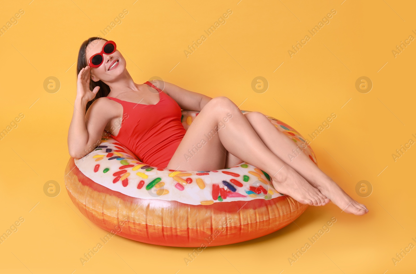 Photo of Beautiful woman in swimsuit with inflatable ring on yellow background