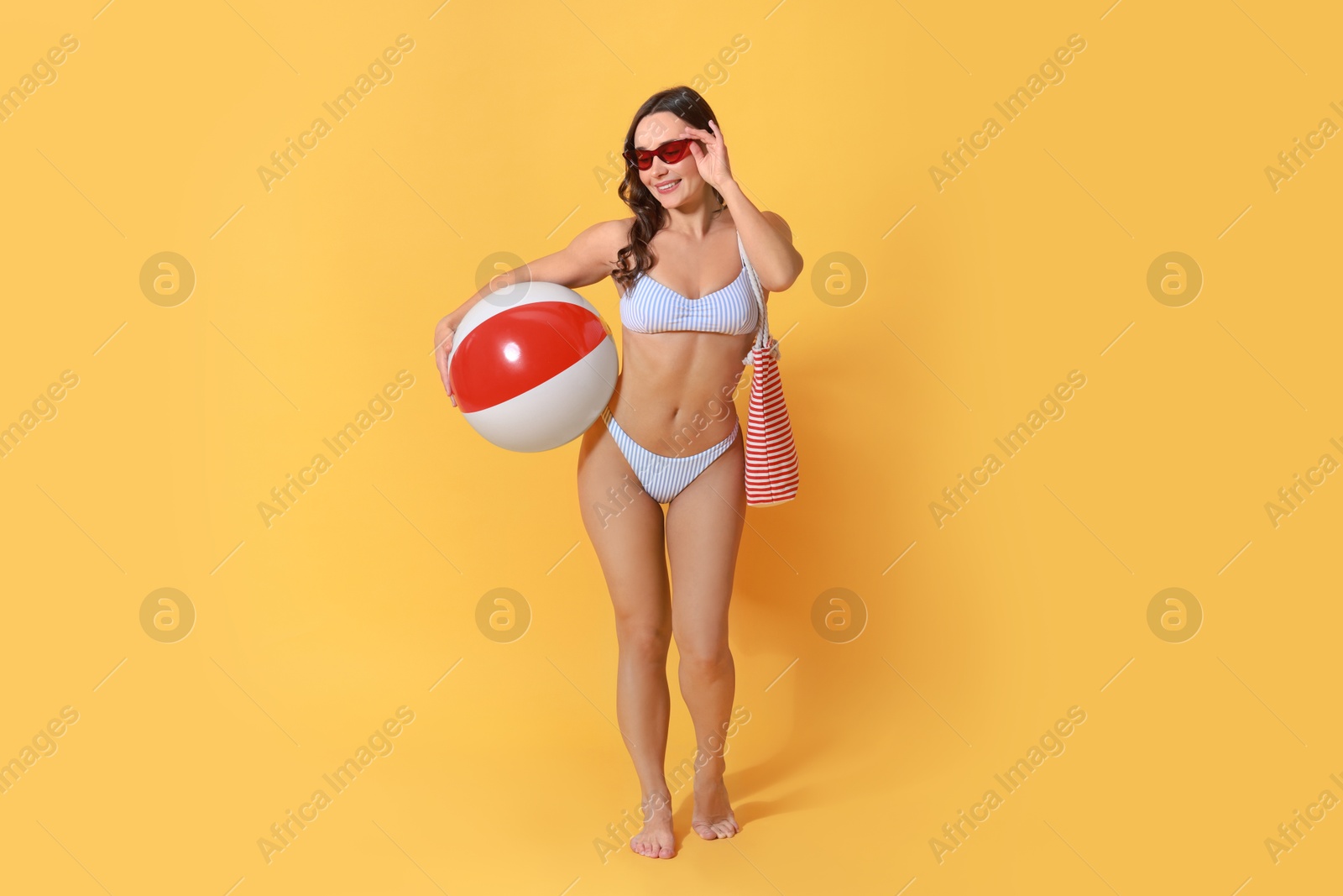 Photo of Beautiful woman in swimsuit with inflatable ball on yellow background