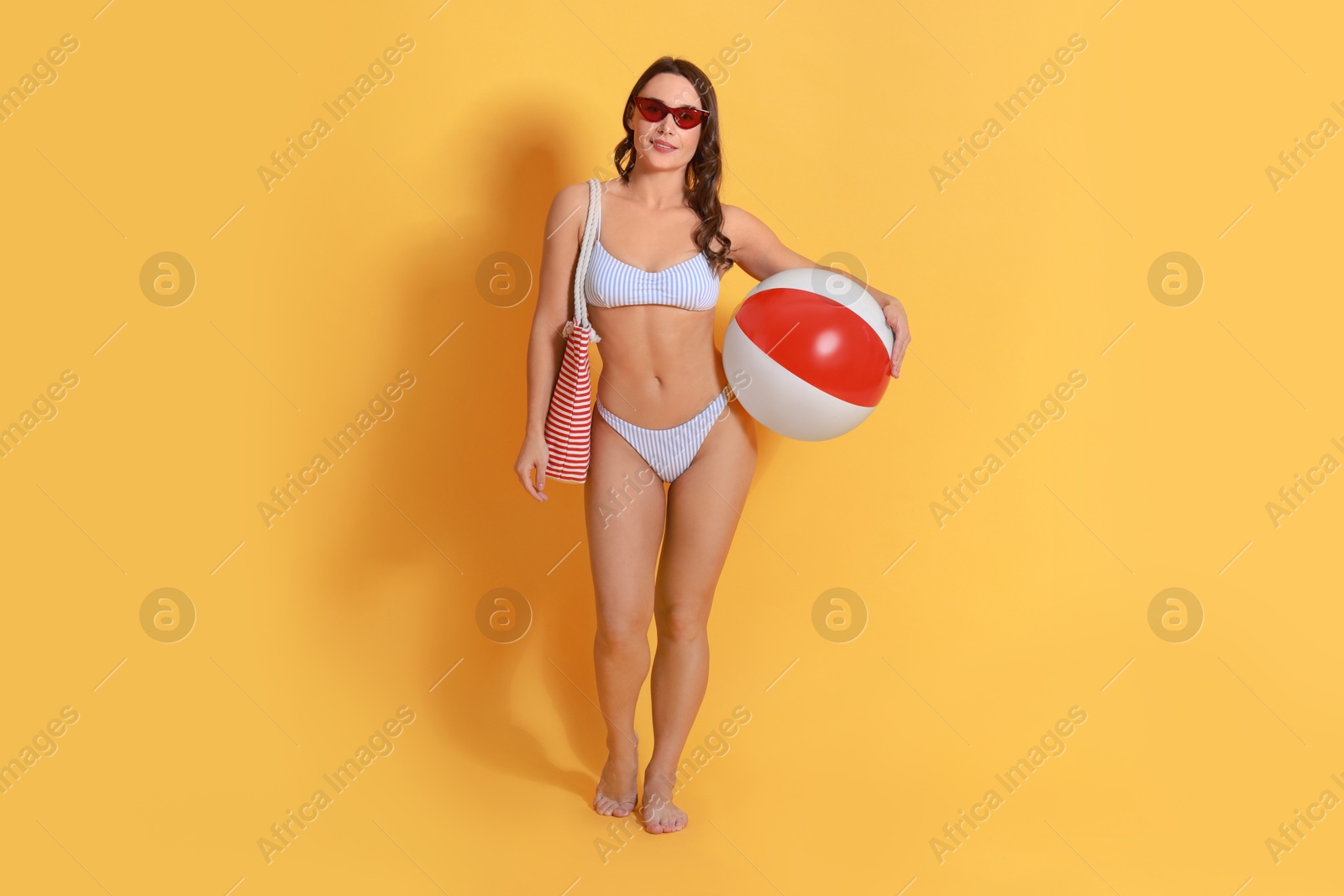 Photo of Beautiful woman in swimsuit with inflatable ball on yellow background