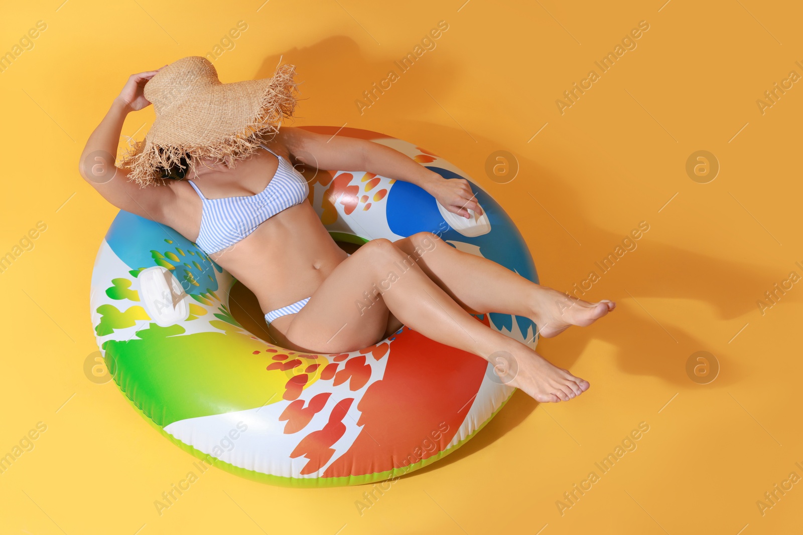 Photo of Beautiful woman wearing swimsuit and straw hat with inflatable ring on yellow background