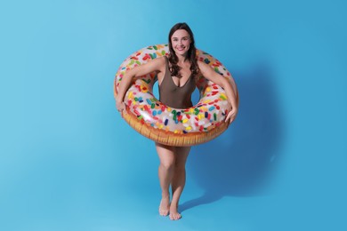 Photo of Beautiful woman in swimsuit with inflatable ring on light blue background