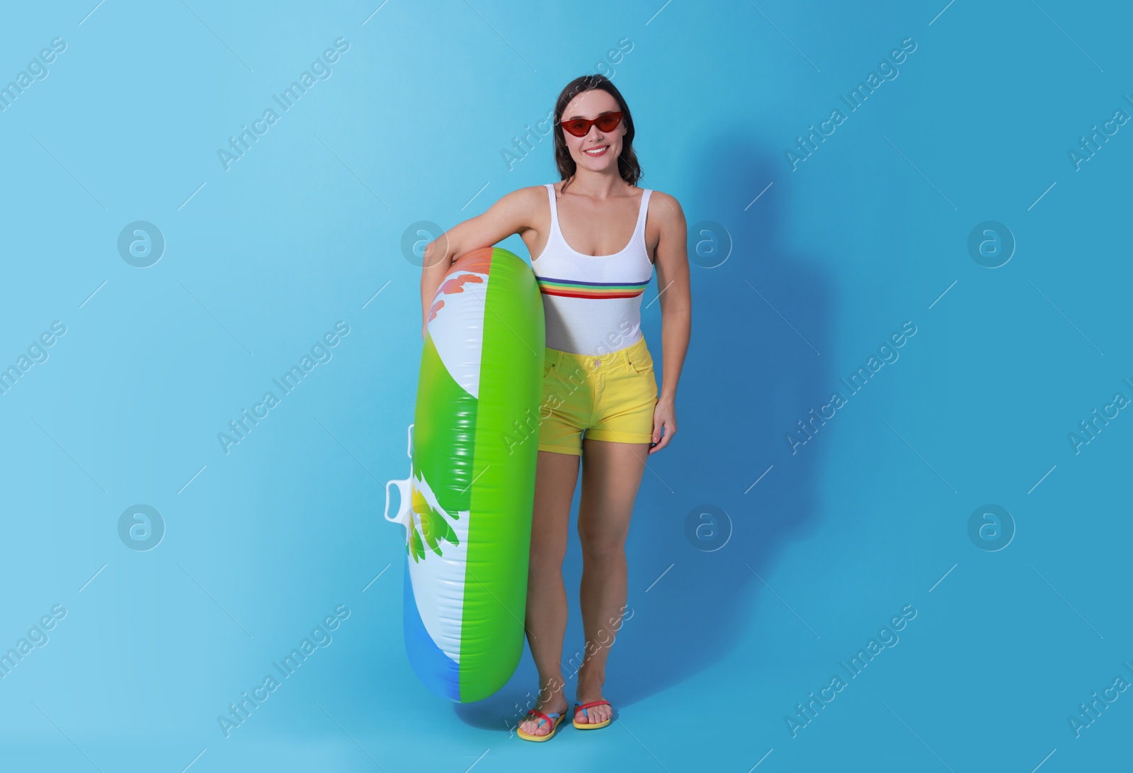 Photo of Beautiful woman in swimsuit with inflatable ring on light blue background