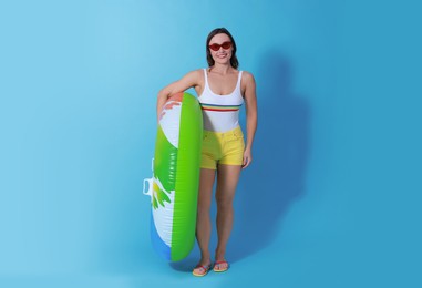 Beautiful woman in swimsuit with inflatable ring on light blue background