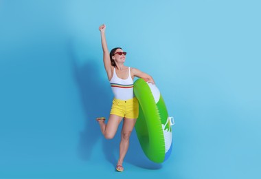 Beautiful woman in swimsuit with inflatable ring on light blue background