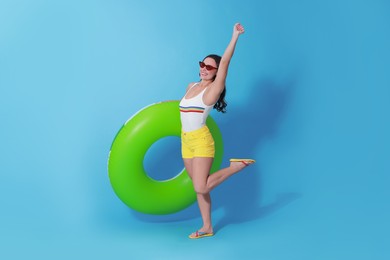 Photo of Beautiful woman in swimsuit with inflatable ring on light blue background