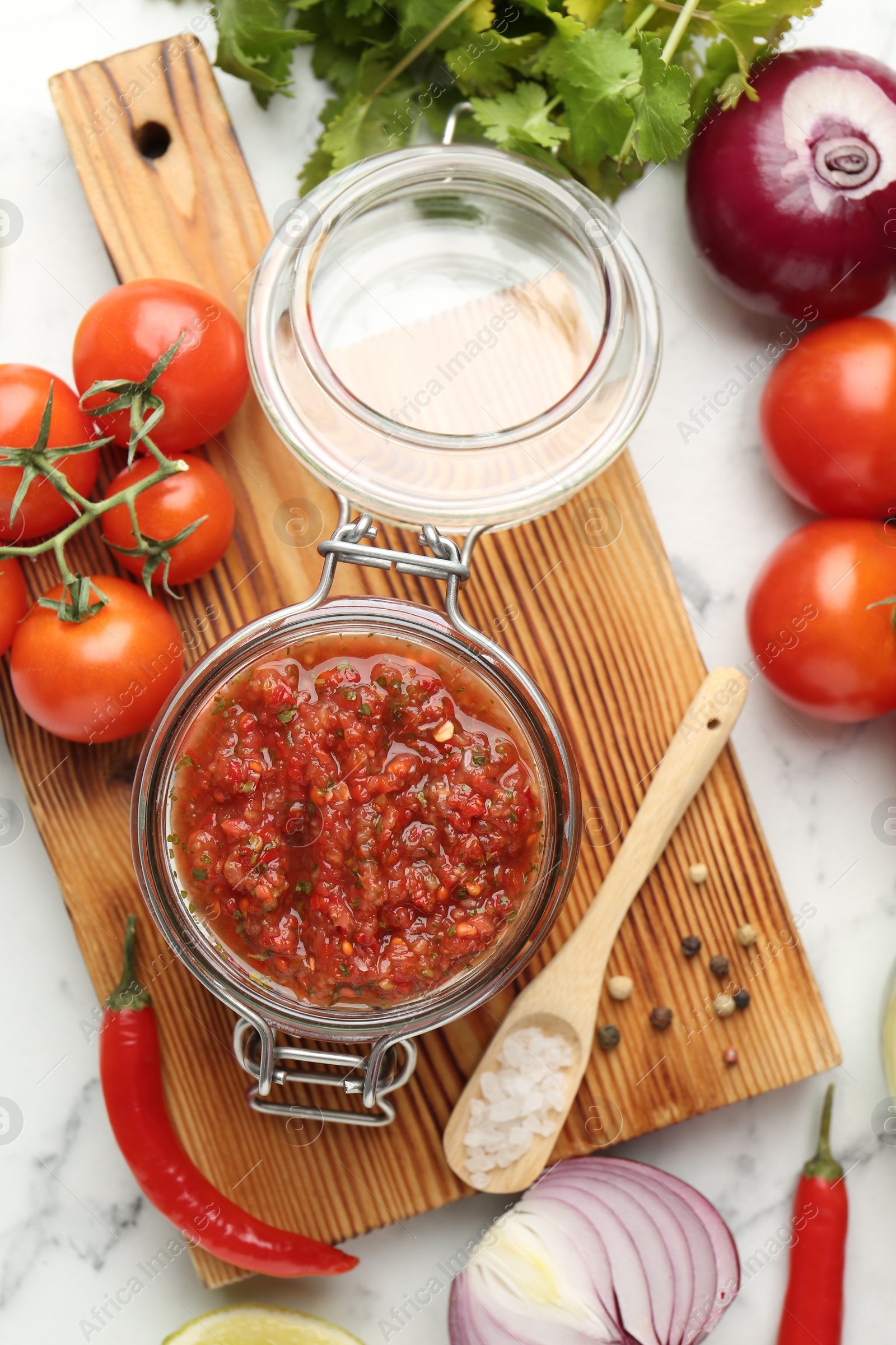 Photo of Spicy salsa and ingredients on white marble table, flat lay