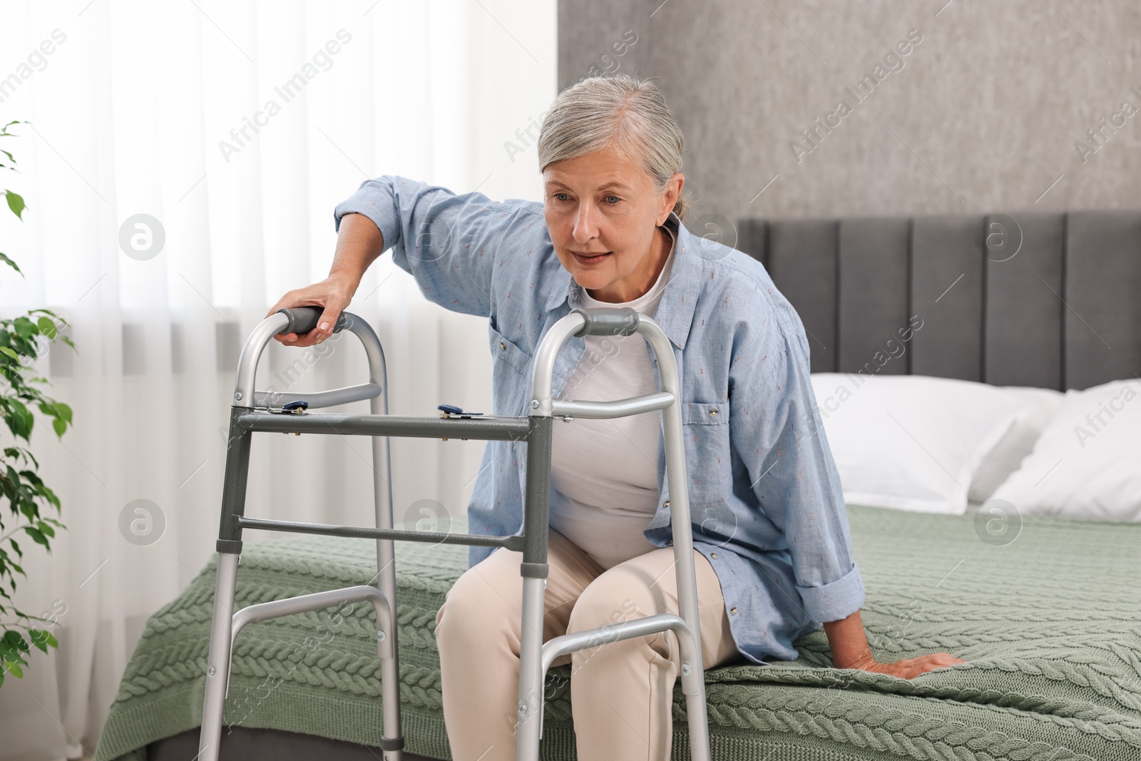 Photo of Senior woman with walking frame on bed at home