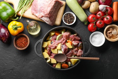 Photo of Cooking stew. Uncooked meat, vegetables and pot on black table, flat lay