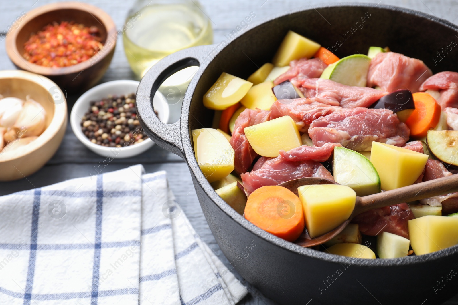 Photo of Cooking stew. Uncooked meat and vegetables in pot on light grey wooden table, closeup