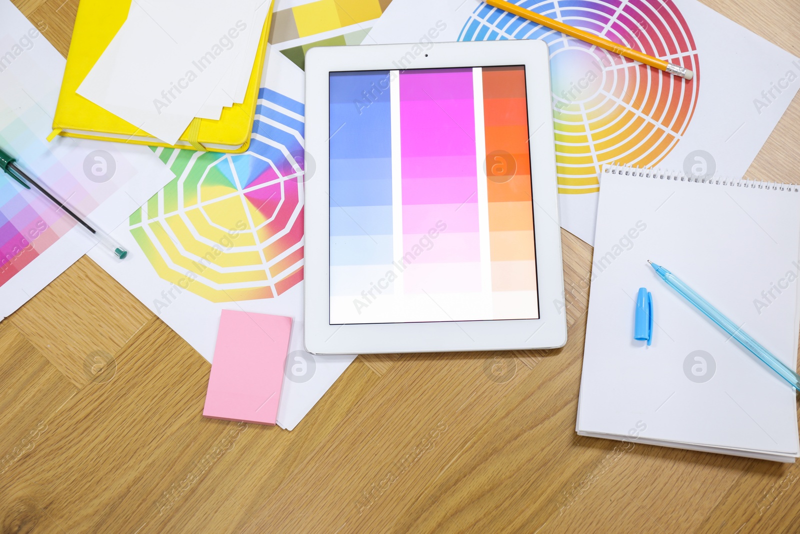 Photo of Designer's workplace with tablet, palettes and stationery on wooden table, flat lay