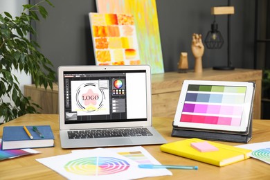 Photo of Designer's workplace with laptop, tablet, stationery and palettes on wooden table indoors