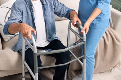 Photo of Nurse helping senior man with walking frame indoors, closeup