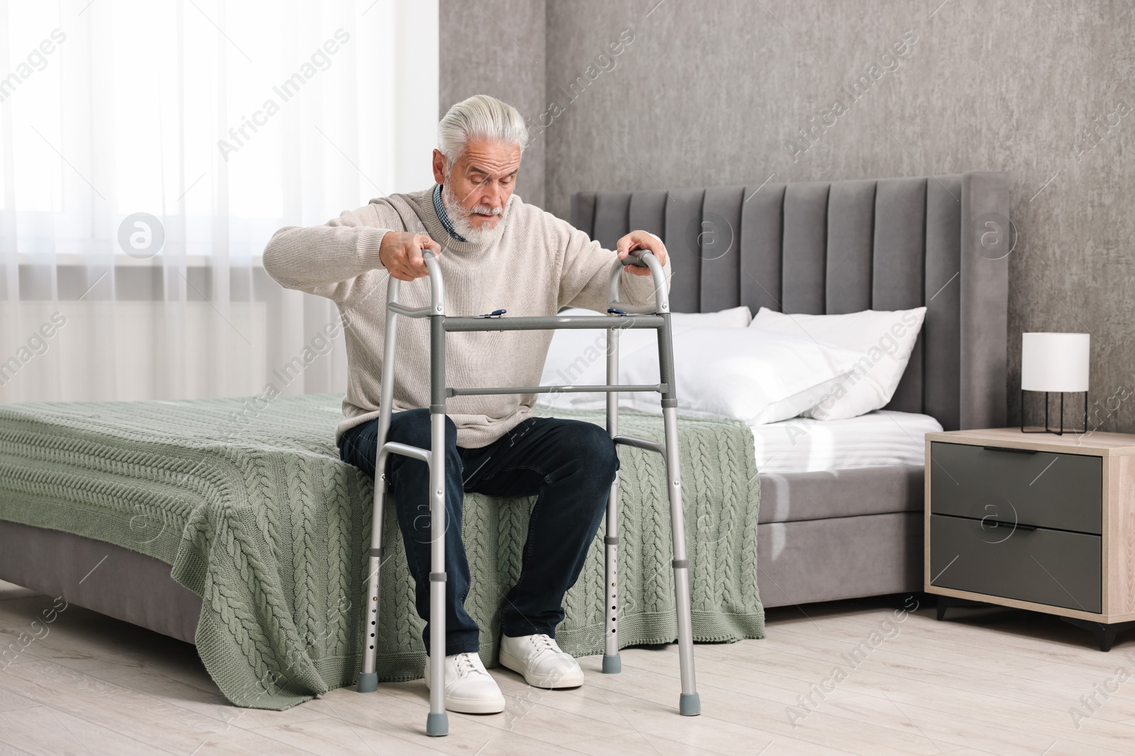 Photo of Senior man with walking frame on bed at home