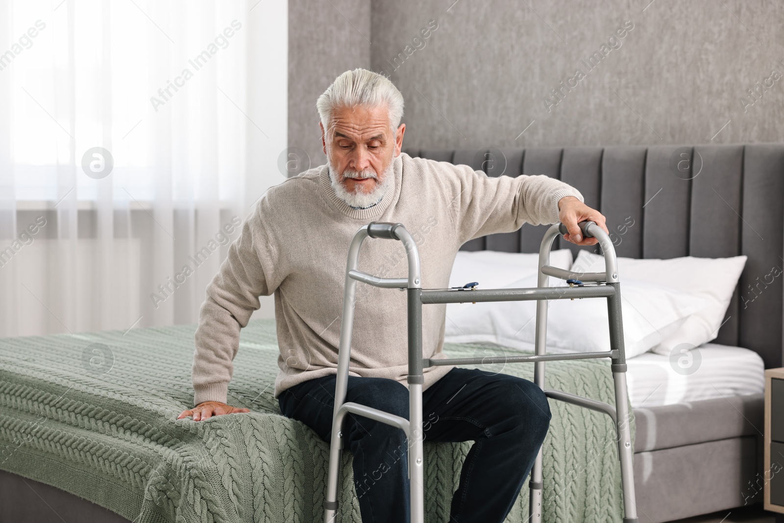 Photo of Senior man with walking frame on bed at home