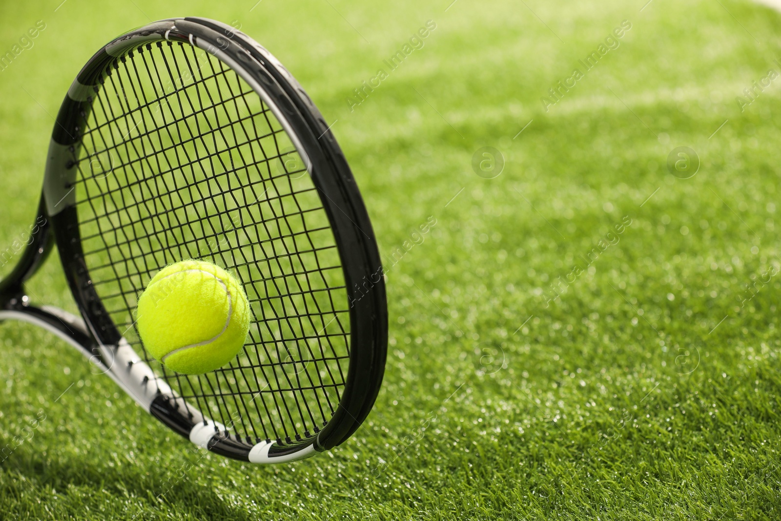 Photo of Tennis racket with ball on green artificial grass, closeup. Space for text