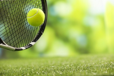 Photo of Tennis racket with ball on green artificial grass, closeup. Space for text