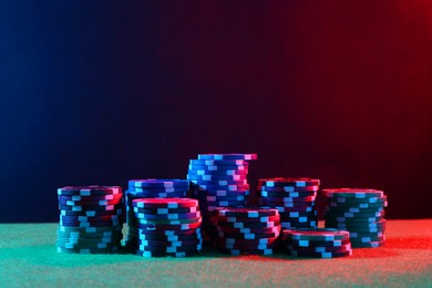 Photo of Poker game. Casino chips on green table in neon lights