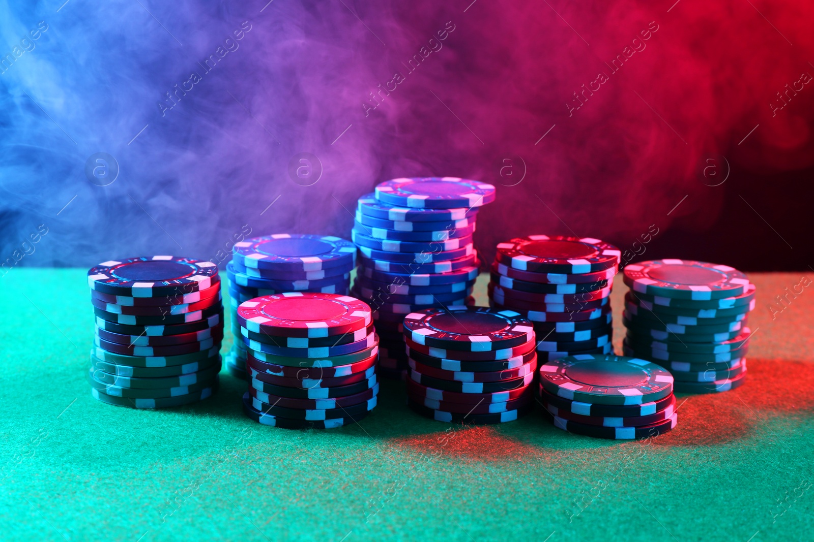 Photo of Poker game. Casino chips on green table in neon lights