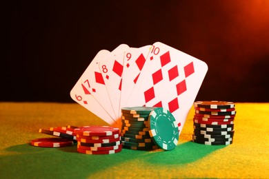 Poker chips and playing cards on green table in neon lights