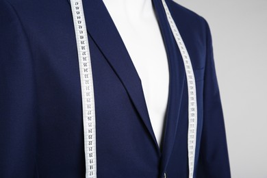 Male mannequin with elegant suit jacket and measuring tape on grey background, closeup