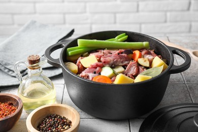 Photo of Cooking stew. Uncooked meat and vegetables in pot on white tiled table