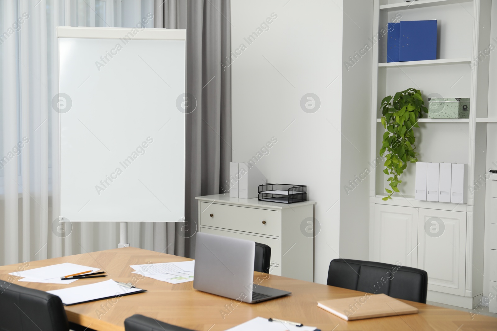 Photo of Flip chart, wooden table and chairs in conference room. Mockup for design