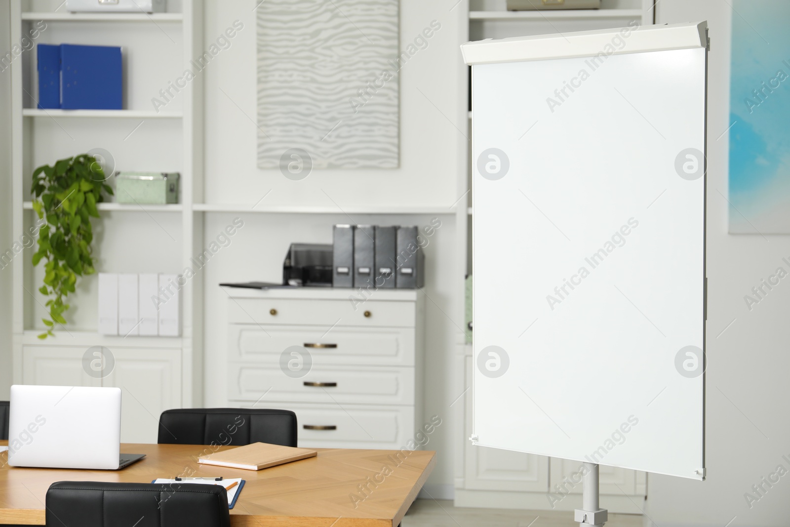 Photo of Flip chart, wooden table and chairs in conference room. Mockup for design