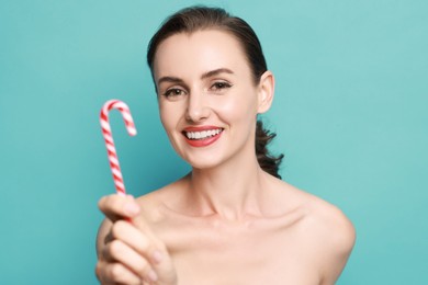 Photo of Smiling woman with perfect makeup holding Christmas candy cane on light blue background