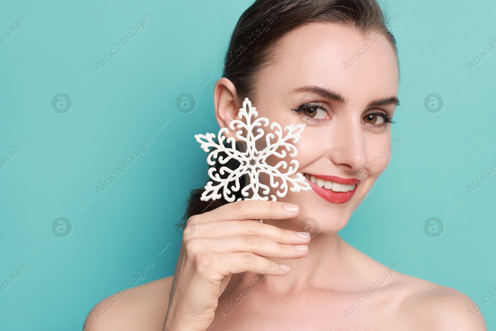 Photo of Smiling woman with perfect makeup holding decorative snowflake on light blue background, space for text. Christmas celebration