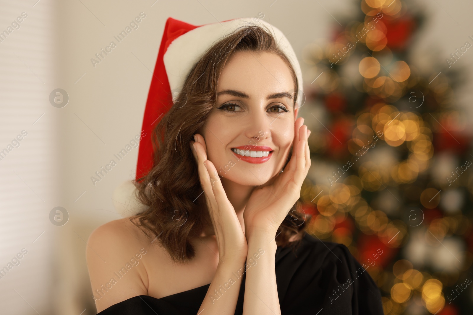 Photo of Smiling woman with perfect makeup in Santa hat celebrating Christmas at home