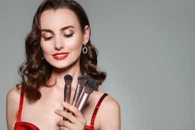 Photo of Smiling woman with different makeup brushes on grey background. Space for text