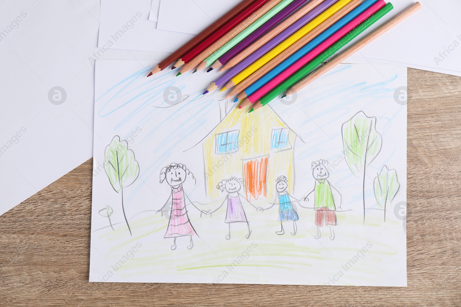 Photo of Child's drawing of happy family and pencils on wooden table, top view