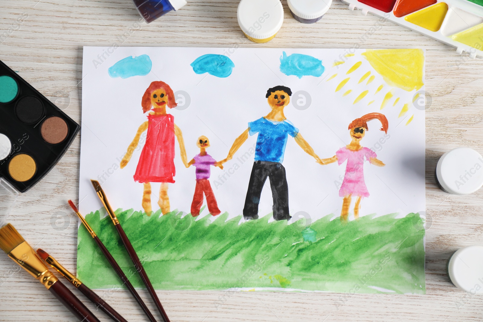 Photo of Child's drawing of happy family and supplies on wooden table, top view