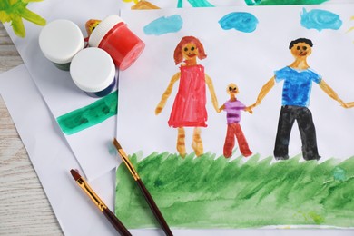 Photo of Child's drawing of happy family and supplies on wooden table, top view