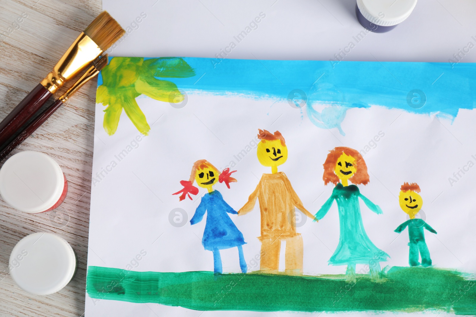 Photo of Child's drawing of happy family and supplies on wooden table, top view