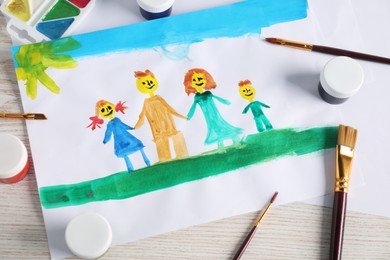 Photo of Child's drawing of happy family and supplies on wooden table, top view