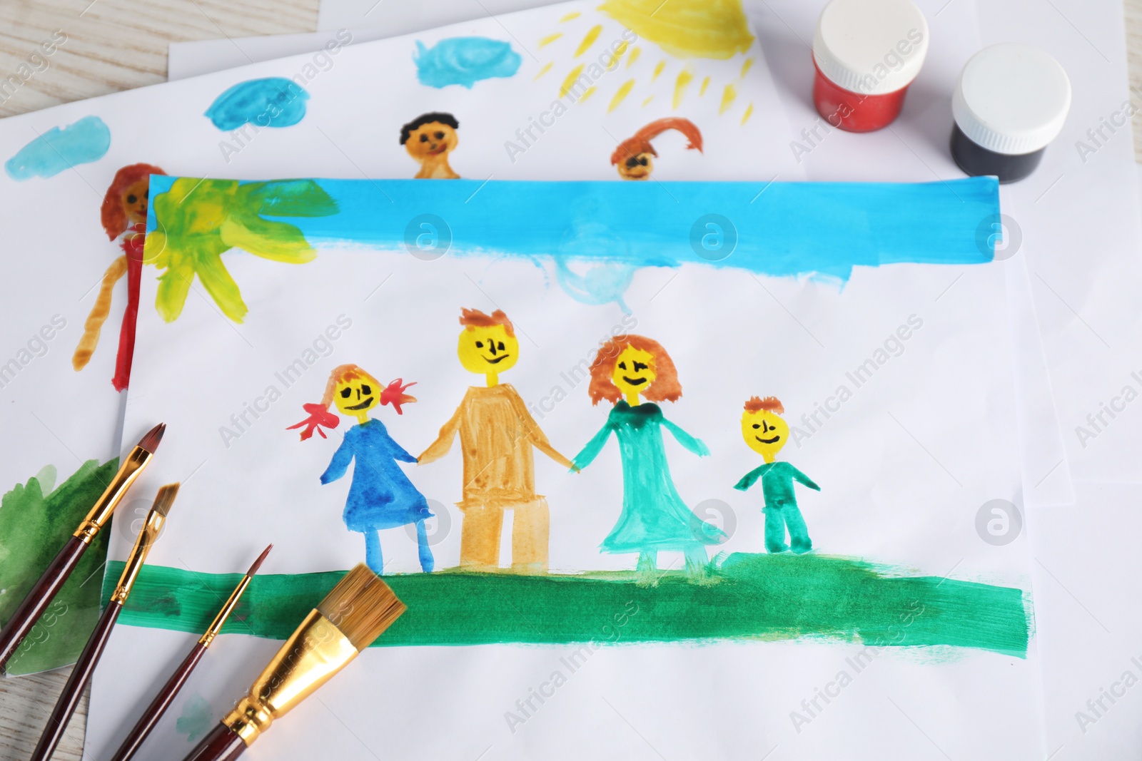 Photo of Child's drawing of happy family and supplies on wooden table, above view