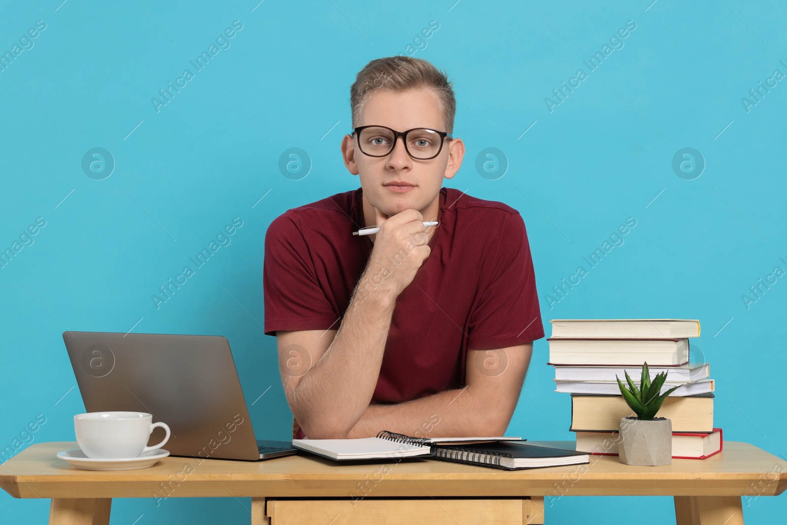 Photo of Preparing for exam. Student with laptop and books at table against light blue background