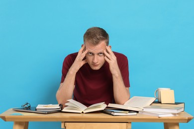 Photo of Preparing for exam. Student with books at table against light blue background