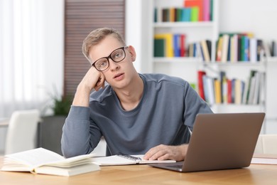 Photo of Preparing for exam. Student with laptop and book at table indoors